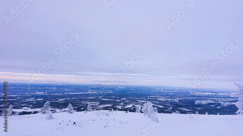 Early morning sunrise in Idre, Sweden with a view from the top of the ski slope and down over the valley with snow covered trees below and mountains in the background. 