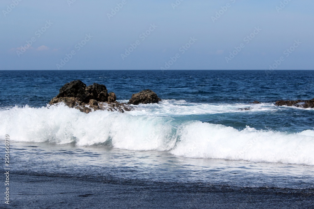 waves crashing on rocks, Waves break on the coastal rock, Black sand beach in Bali, with wave coming to wash it.