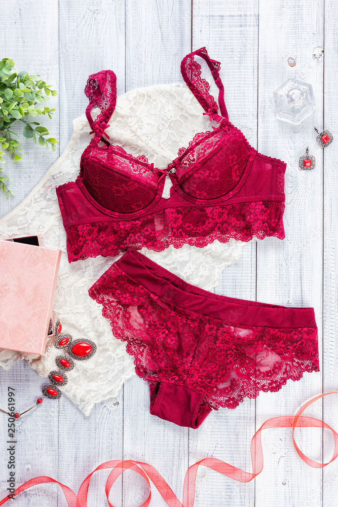 Woman's sexual red lingerie and necklace on white wooden background. Copy space for your text.  Women's lacy underwear pants and brassiere. Top view, flat lay - obrazy, fototapety, plakaty 