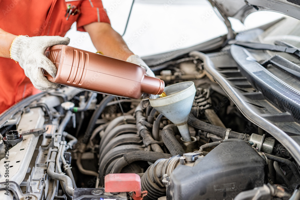 Car mechanic replacing and pouring fresh oil into engine at maintenance repair service station .