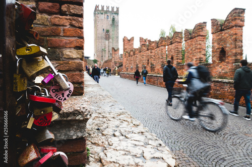 VERONA, ITALY – NOVEMBER 11 2018: People walking and riding bikes on the Castelvecchio Bridge near a lot of locks of love