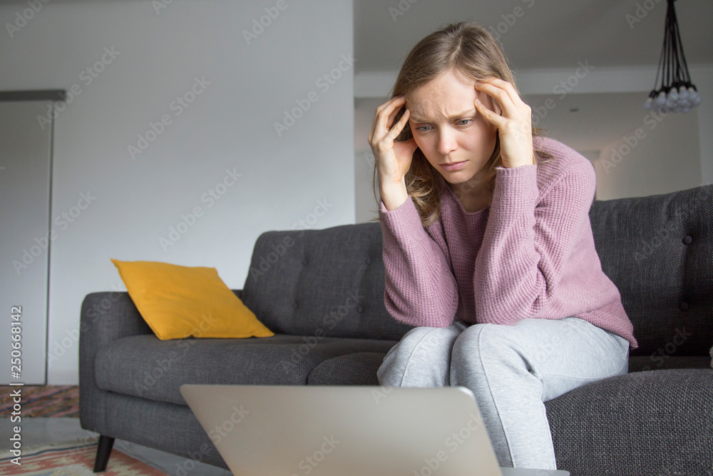 Woman holding fingers on temples, looking at laptop on table Woman holding fingers on temples, looking at laptop on table