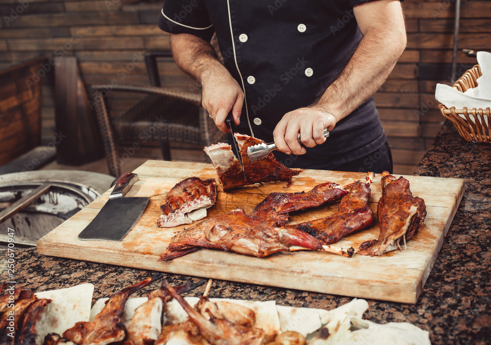 Chef Hands cutting whole grilled lamb for steaks with knife on cutting board. Hot Meat dishes