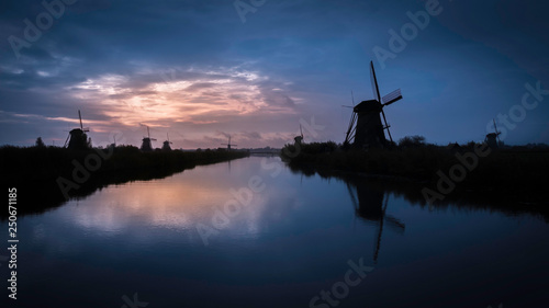Windmills in sunset with a blue and orange sky with reflections in the water in Kinderdijk, The Netherlands