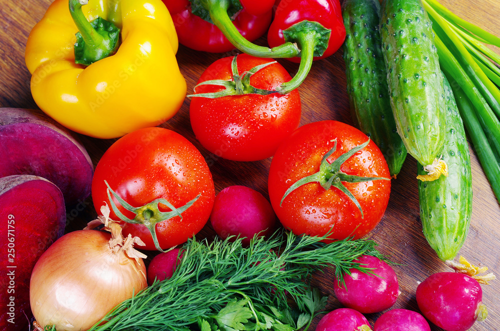 Appetizing vegetables on a wooden table. Tomatoes, cucumbers, radishes, carrots, peppers, parsley.