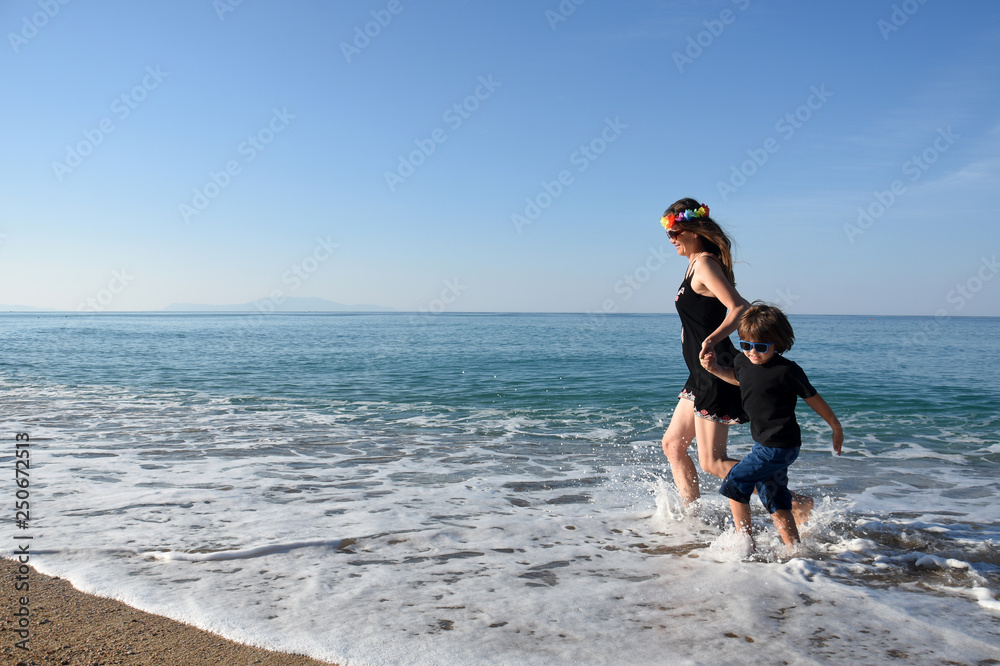 Mother and son playing on the beach. Mom and child holding hands and running to the sea