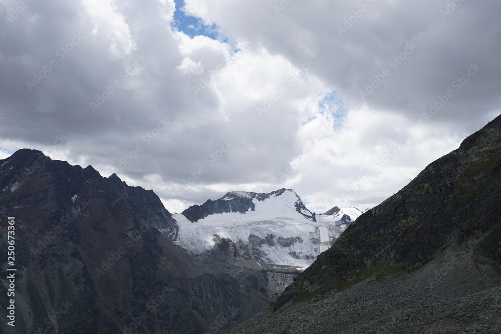 Berglandschaft mit Wolken, Grün, Pflanzen, Felsen und Schnee in Sölden/ Ötztal 