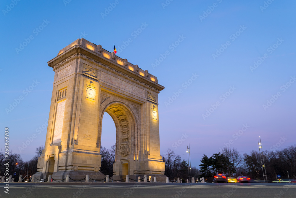 Low angle of Arch of Triumph (Arcul de Triumf) in Bucharest, Romania, at sunset / blue hour. With a height of 27 metres, this arch was inaugurated on 1 December 1936 and it's made of stone.