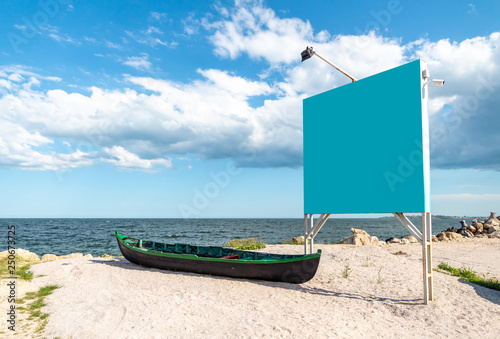 Blue empty billboard next to a local, wooden fishing boat, on the sand, at shore of the Black Sea (Marea Neagra), Romanian coastline. Clear blue Summer sky at the beach. photo