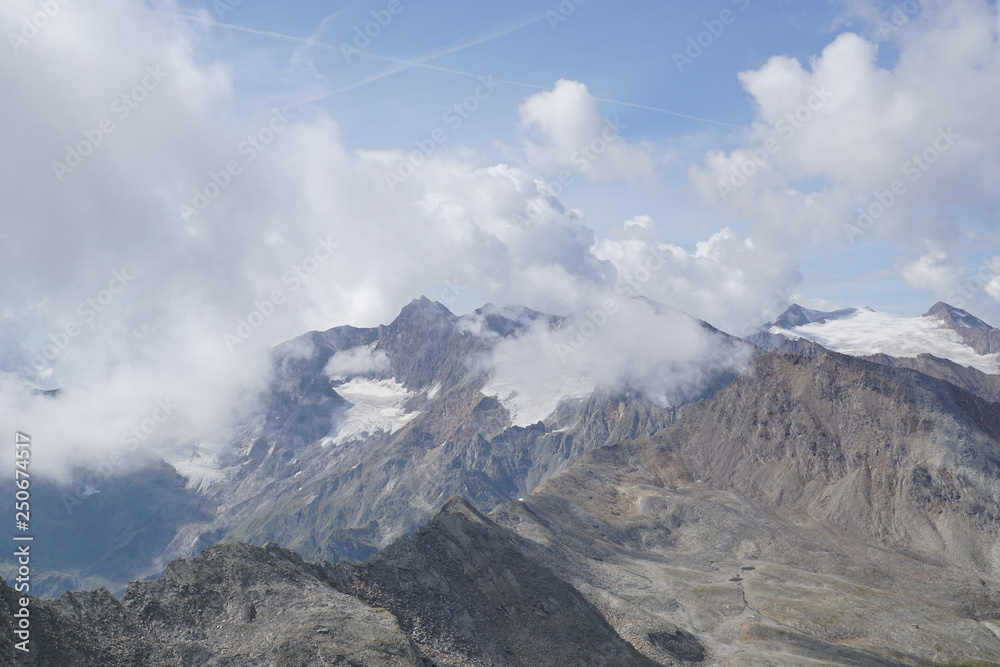 Berglandschaft mit Wolken, Grün, Pflanzen, Felsen und Schnee in Sölden/ Ötztal 