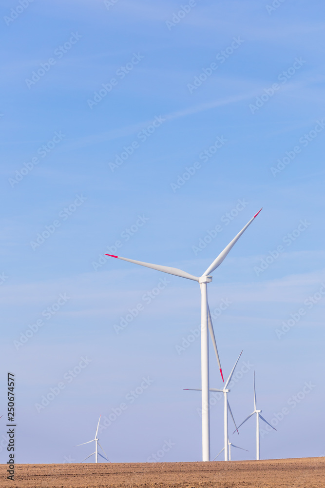 Farm of windmill turbines on agricultural field with blue sky in background. Renewable energy wind turbine Farm of windmill turbines on agricultural field with blue sky in background. Renewable energy wind turbine