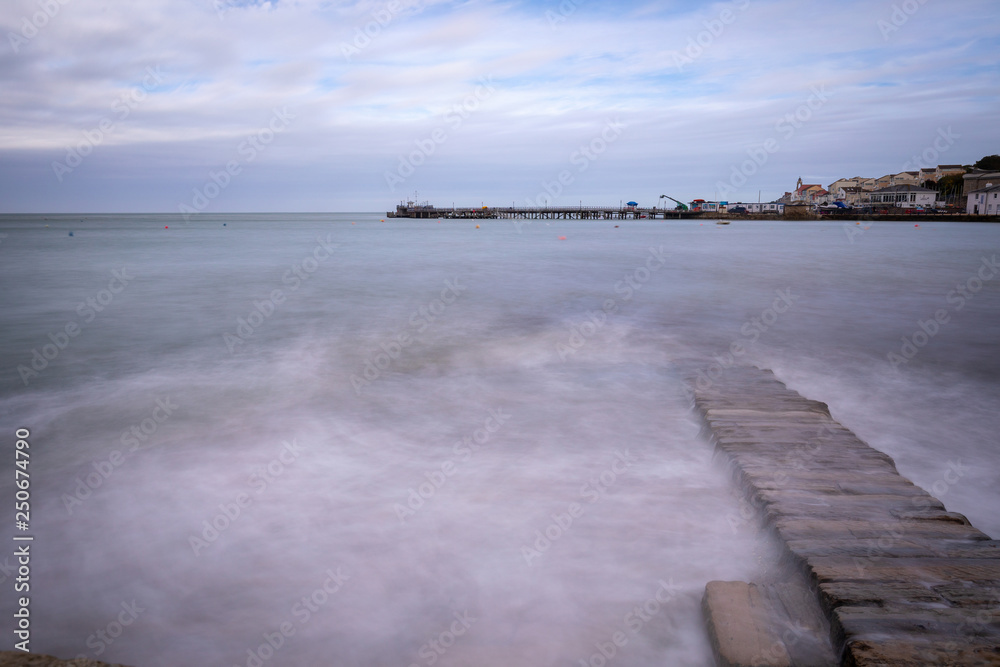 Splashing waves on rock wall in sea with pier