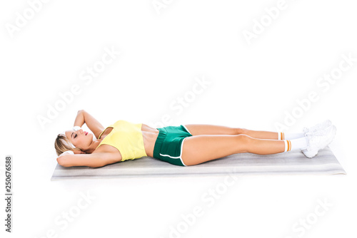 blonde fitness trainer in sportswear exercising on yoga mat isolated on white