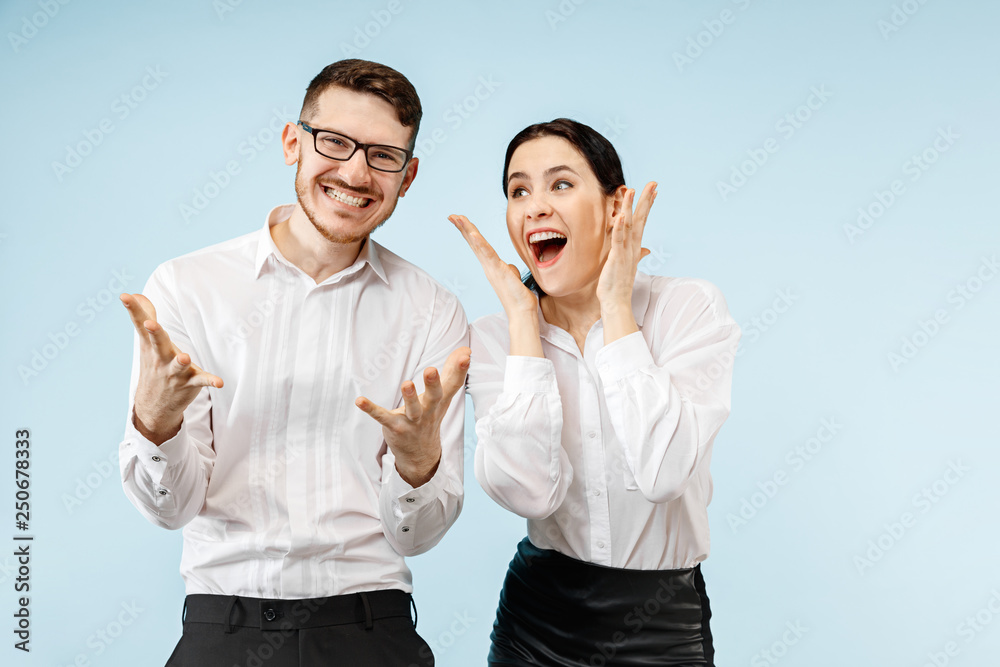 Excited happy young couple looking at camera with delight. Businessman and woman isolated on blue studio background