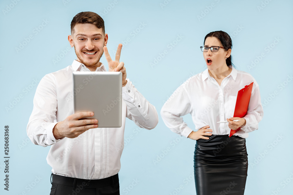 Excited happy young couple looking at camera with delight. Businessman and woman isolated on blue studio background Excited happy young couple looking at camera with delight. Businessman and woman isolated on blue studio background