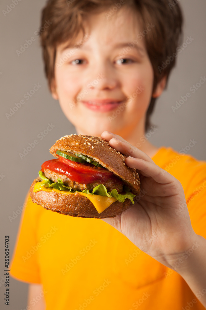 Child eats burger on grey background. Male child with hamburger Child eats burger on grey background. Male child with hamburger