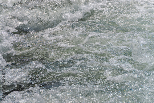 Natural texture of foamed water surface. Rapids of river close-up. Fast flow in mountain creek. Background of clean water waves with copy space. Textured foam of shiny stream. Fast river texture.