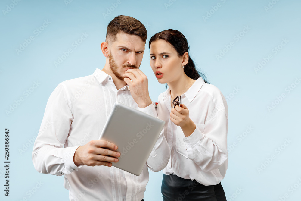 Concept of partnership in business. Young man and woman looking suspicious against blue background at studio Concept of partnership in business. Young man and woman looking suspicious against blue background at studio