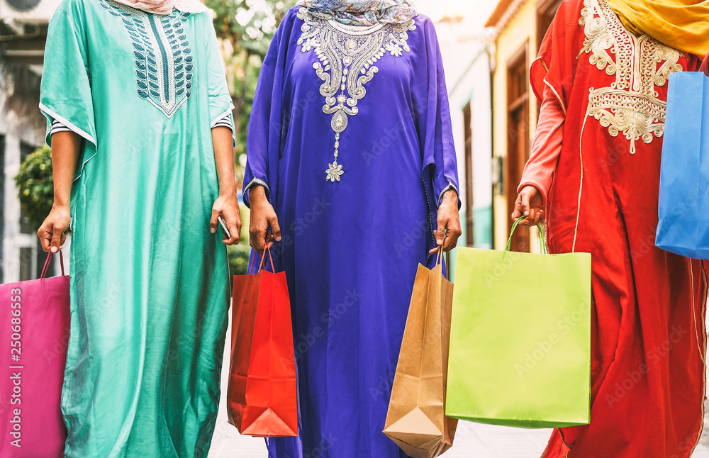Happy Muslim women doing shopping in the city center - Arabian teen girls having fun buying new traditional Arab clothes in mall - Concept of people religion, shopper, consumerism and diverse culture
