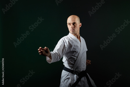 On a dark green background, an active athlete does formal karate exercises
