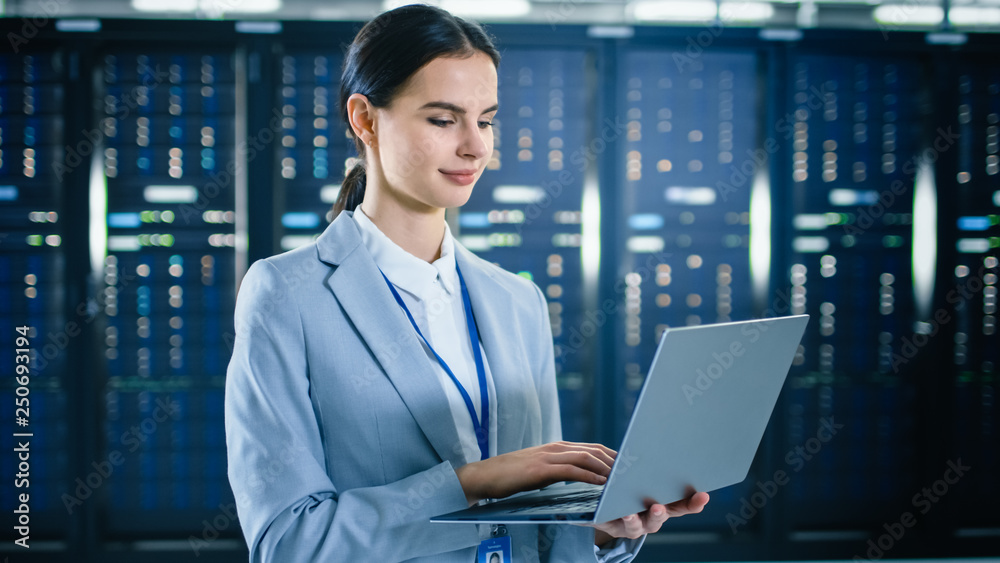Female IT Specialist is Working on Laptop in Data Center Next to Server Racks. Female IT Specialist is Working on Laptop in Data Center Next to Server Racks.