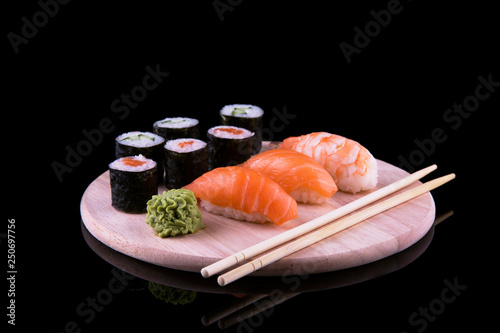 set of sushi on a wooden board with leaves of plants on a dark background