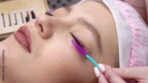 Eyelash Extension Procedure. Woman Eye with Long false Eyelashes. Closeup macro shot of fashion eyes in beauty salon. Hands beautician. Eyelash wizard brushes client's eyelashes with a brush photo