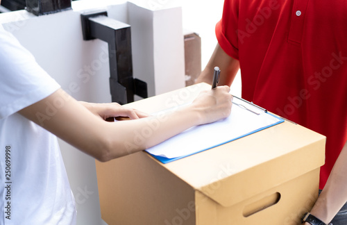 Close-up of a Asian woman appending signature sign on clipboard after accepting receive boxes from delivery man, woman sign on the box, receive delivery concept. photo