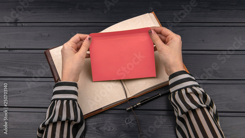 Woman hands holding envelope, notebook page and pen on the wooden desk photo