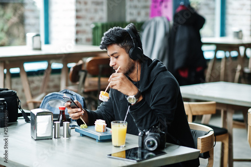 Casual and stylish young asian man with earphones at cafe eating sushi.