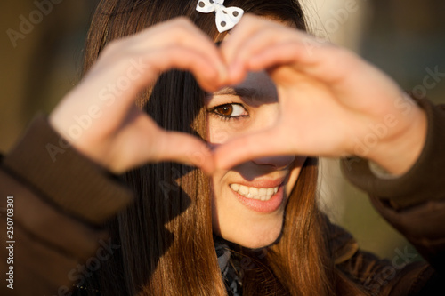 young girl making heart shape hands and smiling at camera