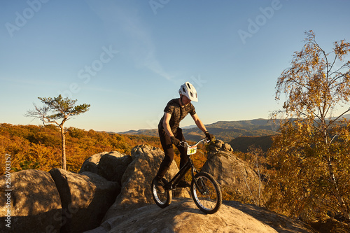 Wallpaper Mural Young male cyclist balancing on trial bicycle on top of big boulder, rider making acrobatic stunt on summer evening, blue sky and forest on background. Concept of extreme sport active lifestyle Torontodigital.ca