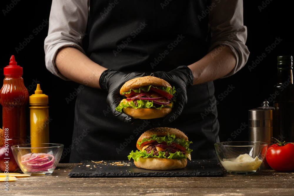 the chef prepares a burger, a hamburger. on a background with ingredients. Delicious and fast food, fast food. A menu, a cafe, fast food, catering, gastronomy - obrazy, fototapety, plakaty 
