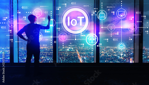 IoT theme with man writing on large windows high above a sprawling city at night