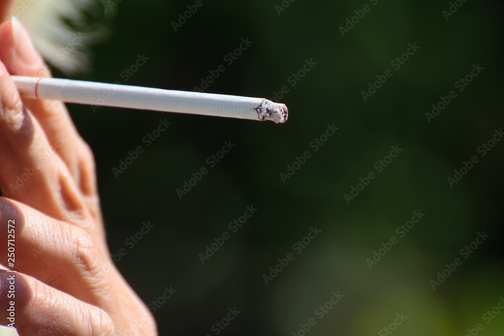 Female fingers smoking cigarette on a green background
