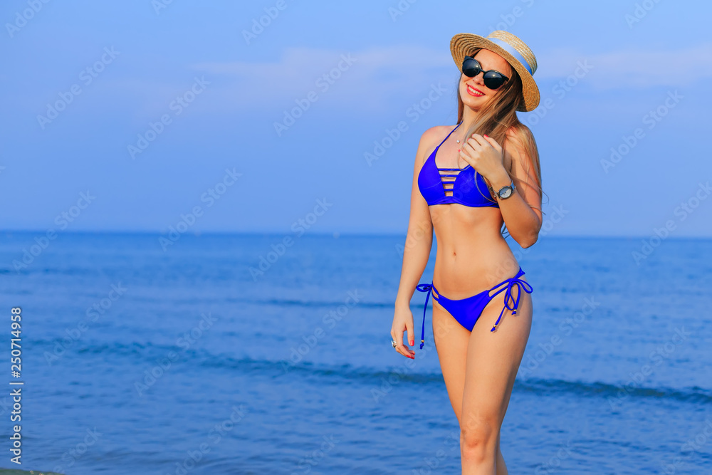 Happy tanned girl in blue swimsuit, on the background blue sea w