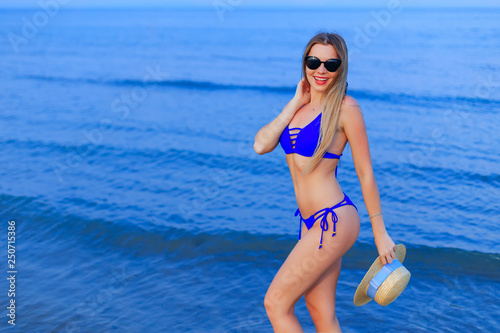 Pretty girl with sunglasses in blue swimsuit poses on the backgr