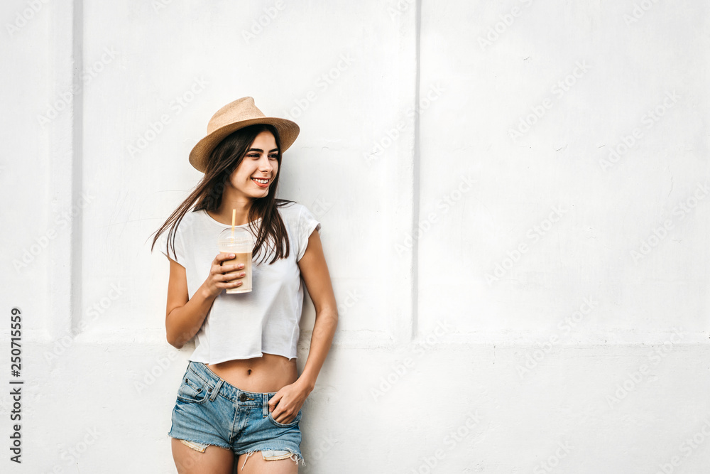 Pretty brunette girl in hat with coffee and white wall behind, copy space. Pretty brunette girl in hat with coffee and white wall behind, copy space.