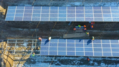 Aerial top view of a group of electricians  in bright helmets installing solar panels at a solar power plant under construction