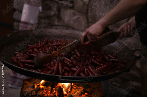 Traditional cooking chef in a cast-iron frying pan. Roasted sausages on an open flame. Cooking for many people. Outdoor cooking in the mountains.