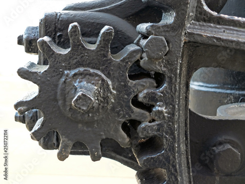a close up of old worn black painted large cog wheels with gear teeth on obsolete industrial machinery