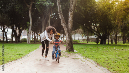 Foto Little boy learning to ride bicycle at park with mother