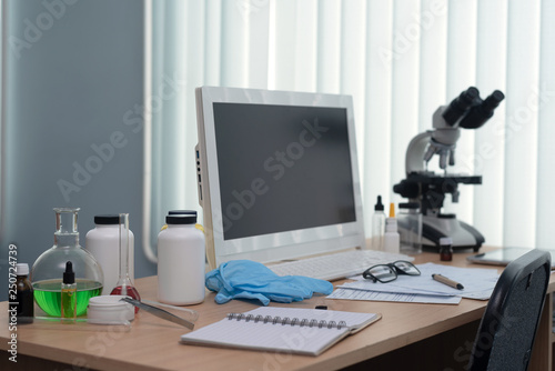 Pharmacology background. Medicine. Laboratory table with a blank screen computer, microscope and various flasks above.