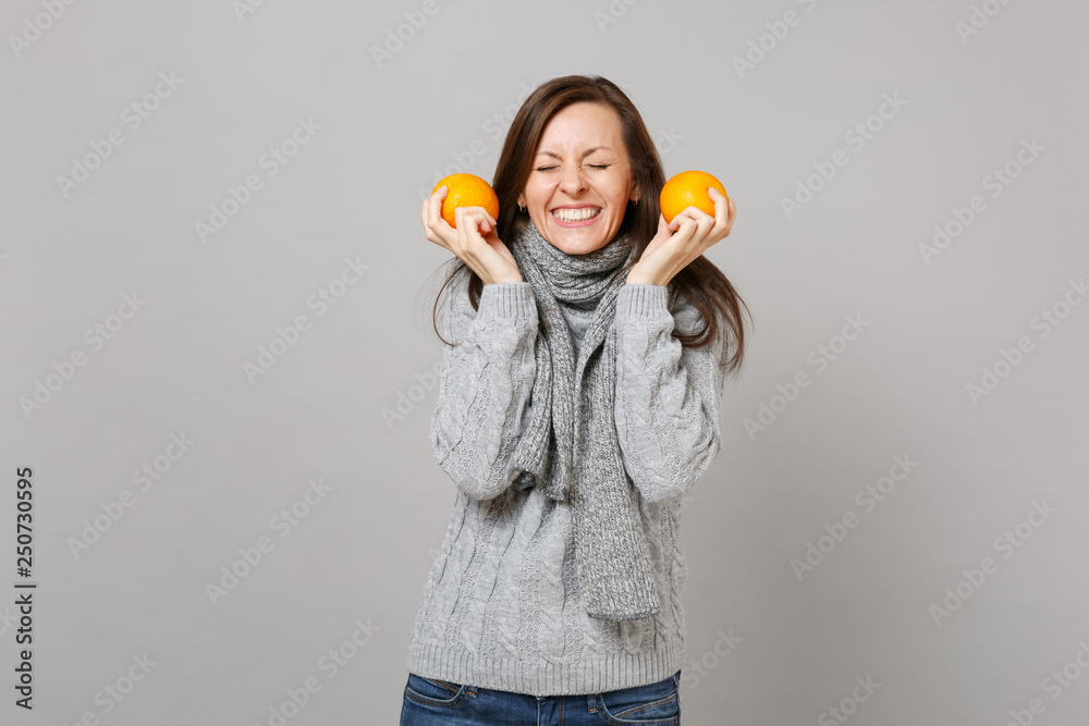 Pretty young woman in gray sweater, scarf with closed eyes holding oranges isolated on grey wall background. Healthy fashion lifestyle people sincere emotions, cold season concept. Mock up copy space. Pretty young woman in gray sweater, scarf with closed eyes holding oranges isolated on grey wall background. Healthy fashion lifestyle people sincere emotions, cold season concept. Mock up copy space.