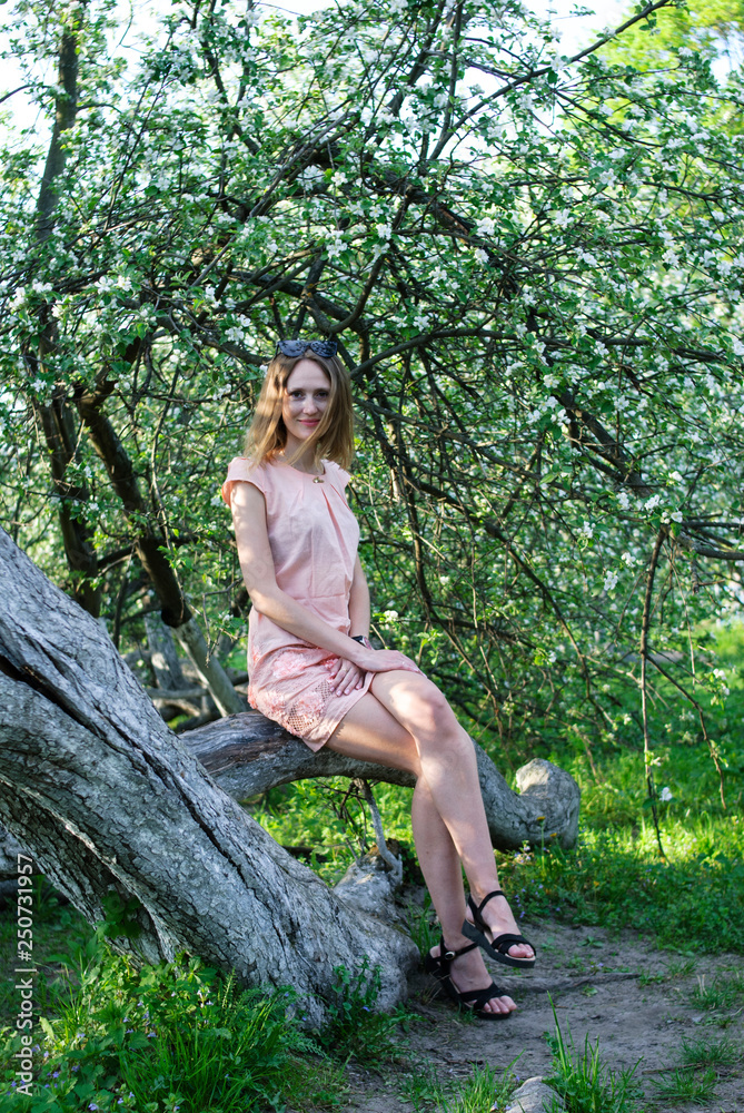 Young beautiful girl stays near an apple tree with wreath made of flowers of apple tree Young beautiful girl stays near an apple tree with wreath made of flowers of apple tree