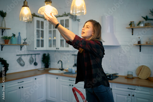 Young woman changing a light bulb at the kitchen