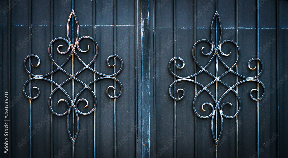 .Wrought iron gate flower like custom made ornament on dark grey metal plate .Wrought iron gate flower like custom made ornament on dark grey metal plate