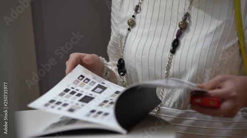 a woman dressed in a white jacket and black beads holding a catalog, flipping it, shooting close-up