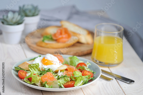 Green salad with lightly salted salmon. On a plate with salad toast with poached egg. In the frame of a glass with orange juice and a plate with bruscheta. Light background. Close-up. 