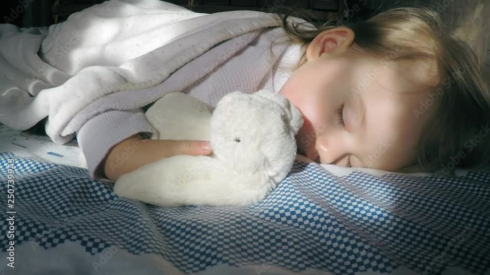 Beautiful little girl with blond hair sleeping on the bed and lit by ...